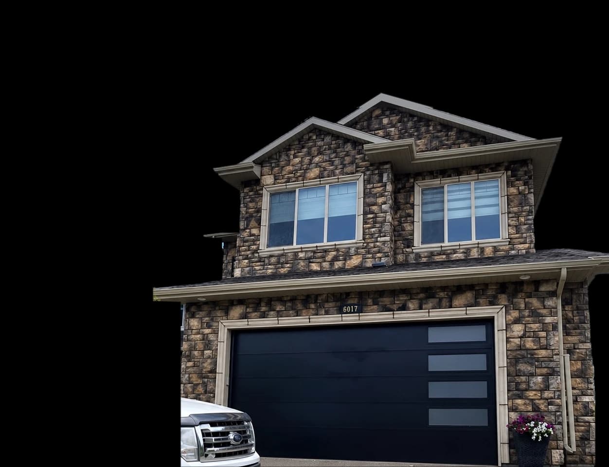 Stone house in Edmonton with a new black modern garage door installed by Asmara